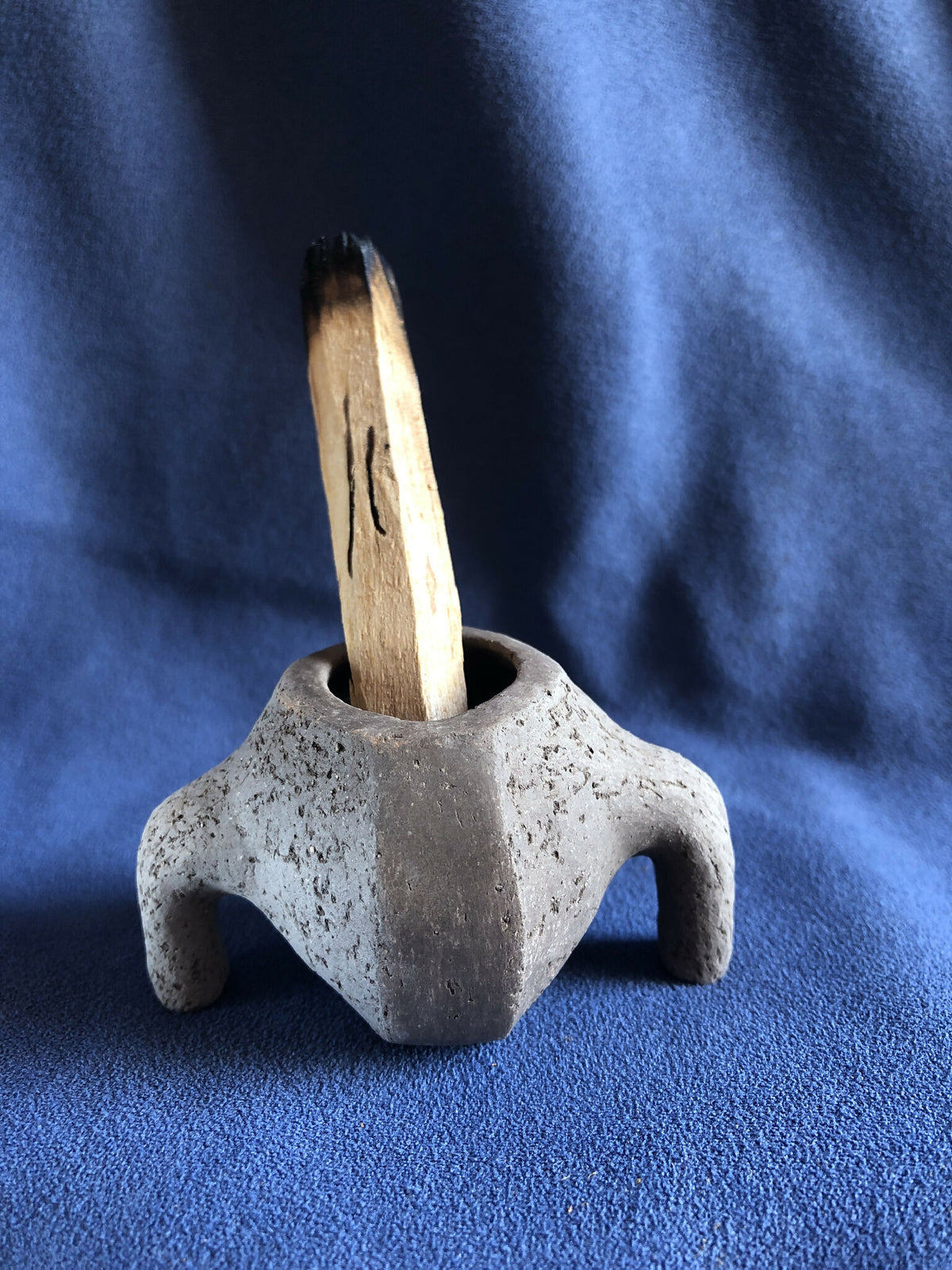 Petit pot en pierre grise avec tige en bois verticale dans l’ouverture.