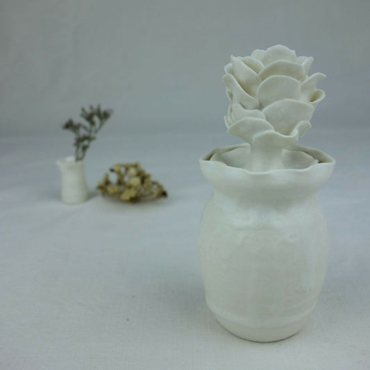 Vase en céramique blanc avec fleurs en relief empilées au centre, vue de profil.