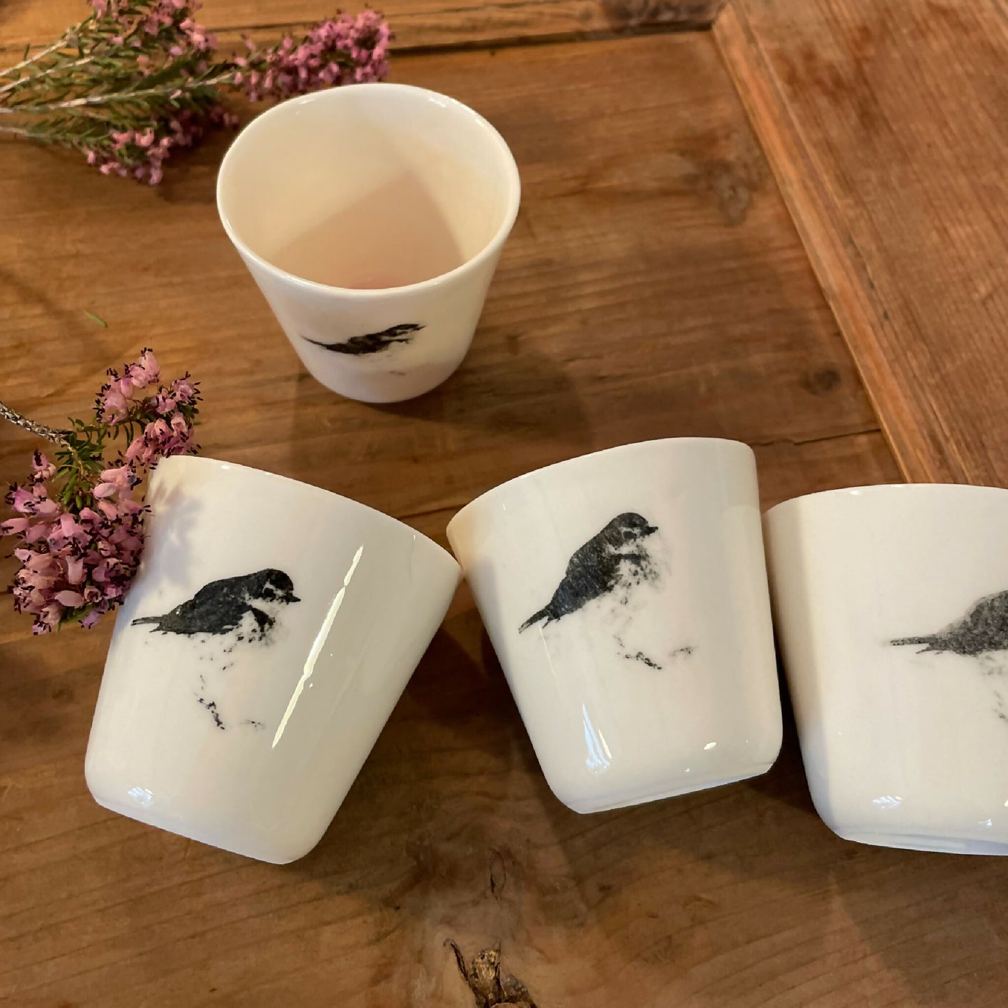 Plusieurs tasses à ristretto blanches avec motifs d’oiseaux noirs, posées autour de fleurs