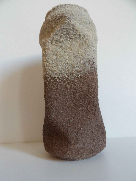 Sculpture cylindrique en surface granuleuse, teinte marron foncé, forme compacte.