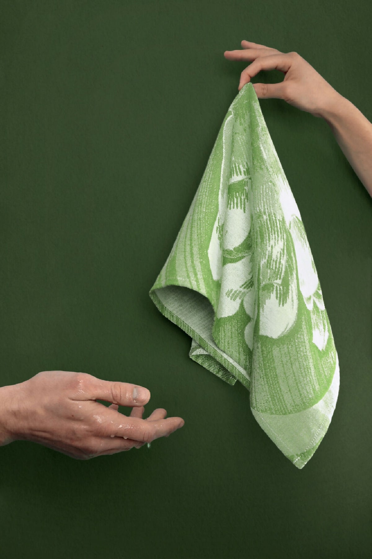 Torchon vert à fleurs blanches, tenu et déplié, tissu texturé