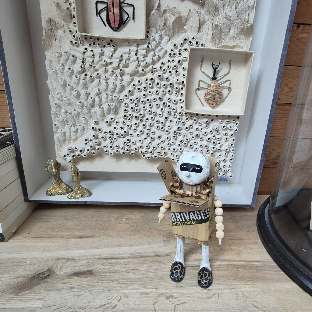 Sculpture bonhomme en carton exposé en vitrine murale, tête blanche et chaussures léopard