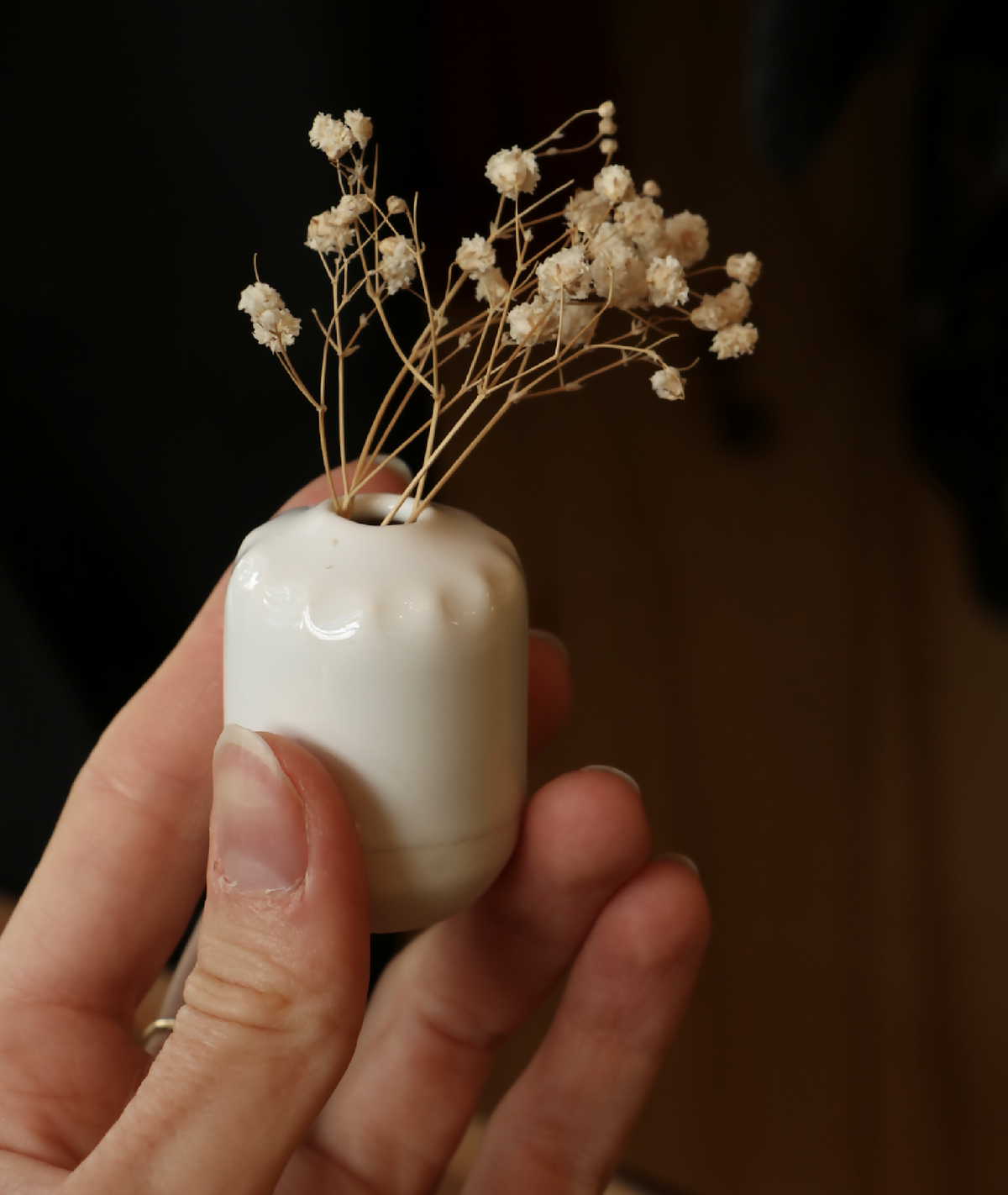 Mini-vase en porcelaine blanche, tenu à la main, surface brillante et col étroit.