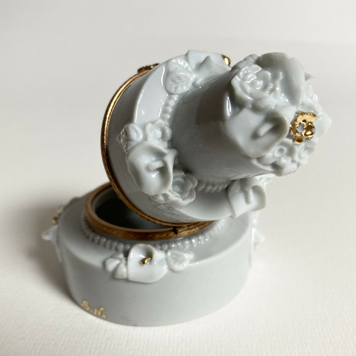Boîte en porcelaine blanche ouverte, gros plan sur décor floral et accent doré.