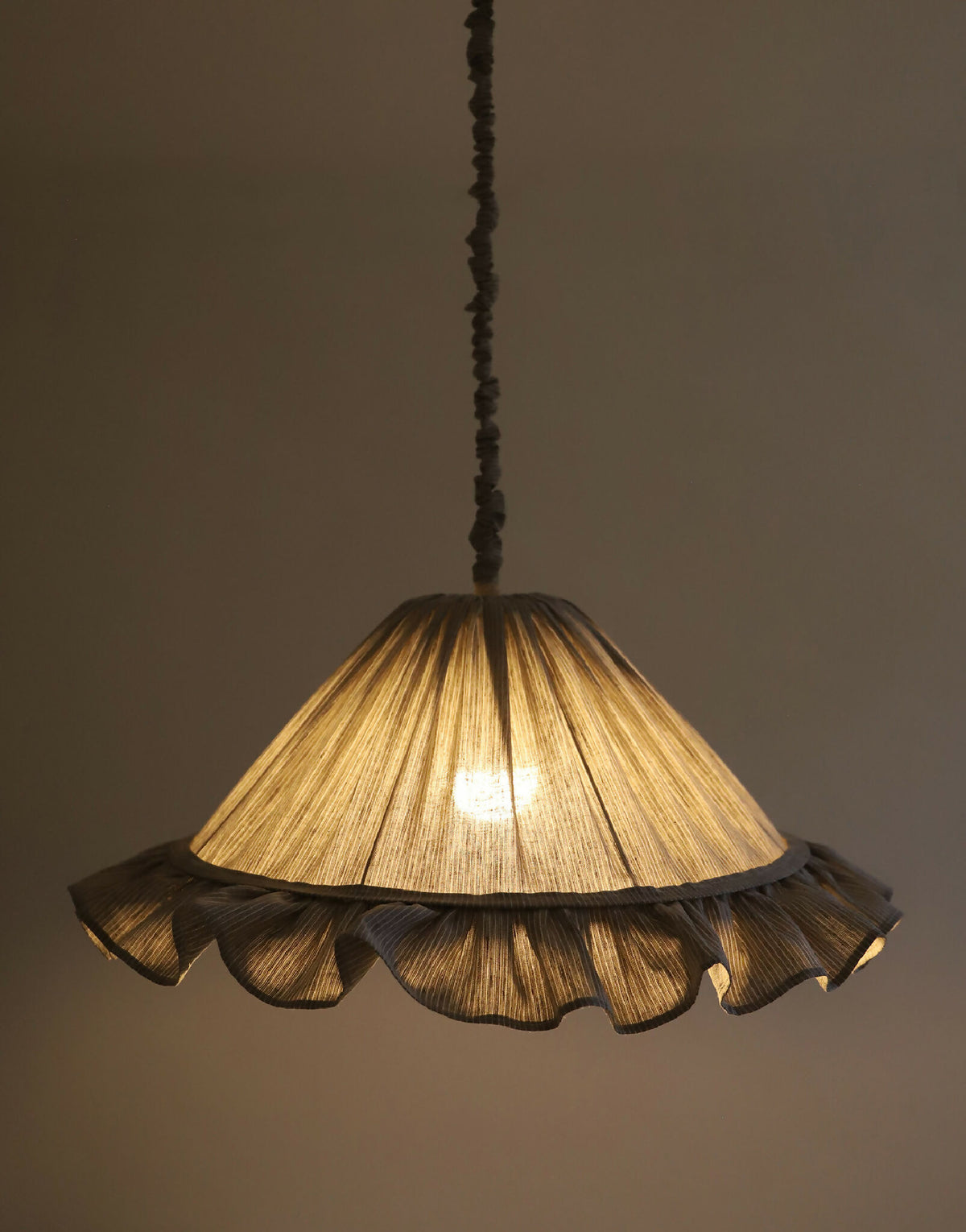 Abat-jour gris à rayures et volants, intérieur éclairé d’une lumière chaude.