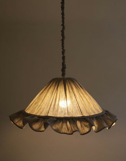 Abat-jour gris à rayures et volants, intérieur éclairé d’une lumière chaude.