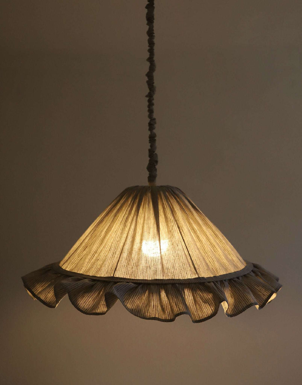 Abat-jour gris à rayures et volants, intérieur éclairé d’une lumière chaude.