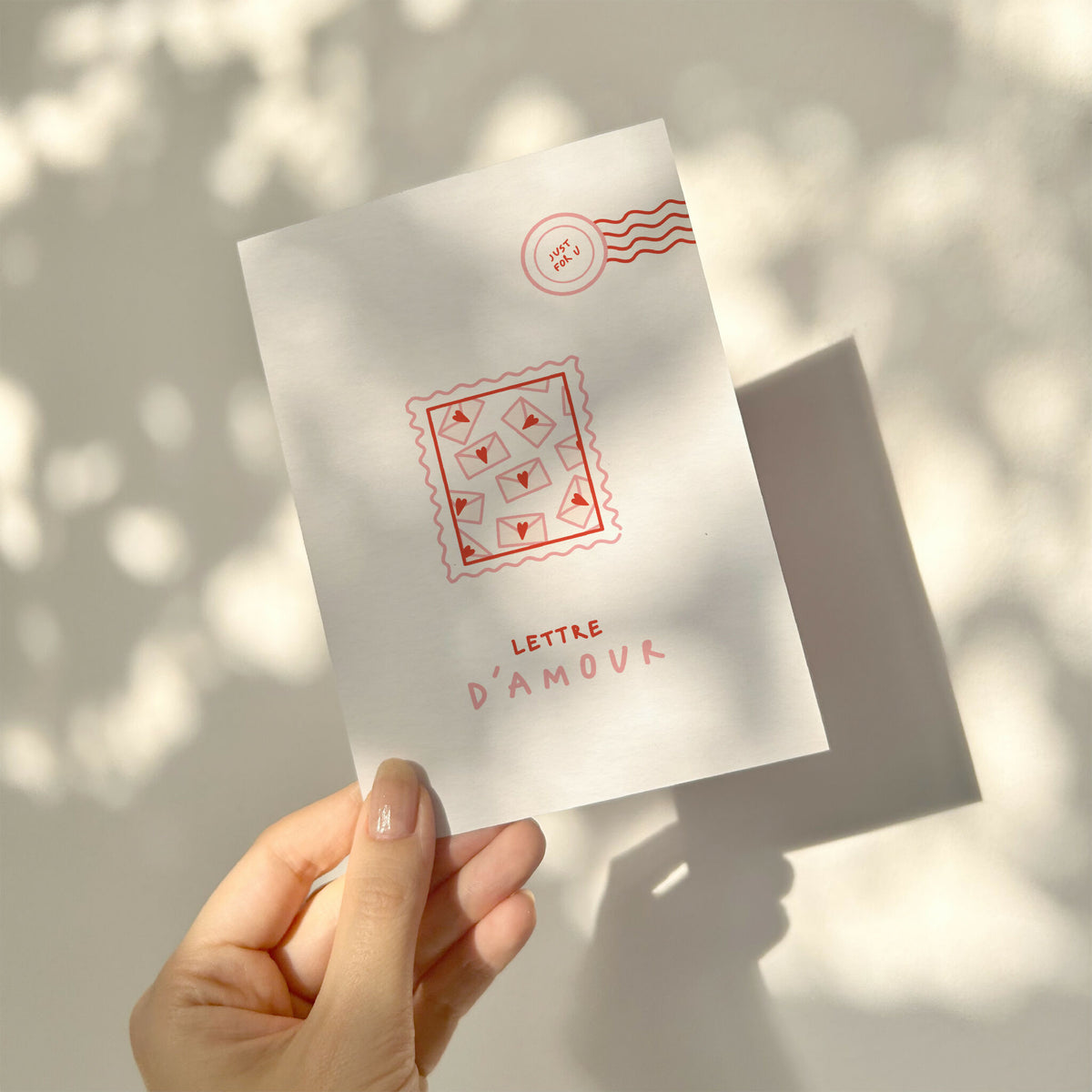 Carte de vœux blanche « Lettre d’amour » tenue par la main, motif d’enveloppes rouges