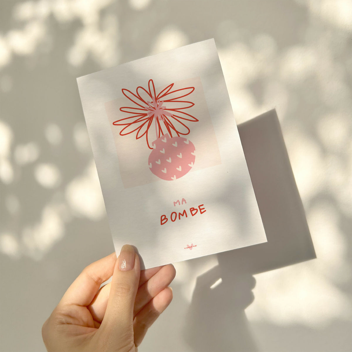 Carte de vœux blanche « Ma Bombe » tenue en main, illustration rouge et texte