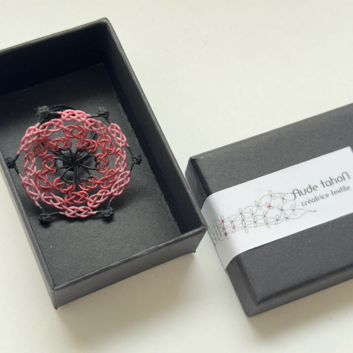 Bague en soie trèfle rouge présentée dans une boîte noire, motif ajouré