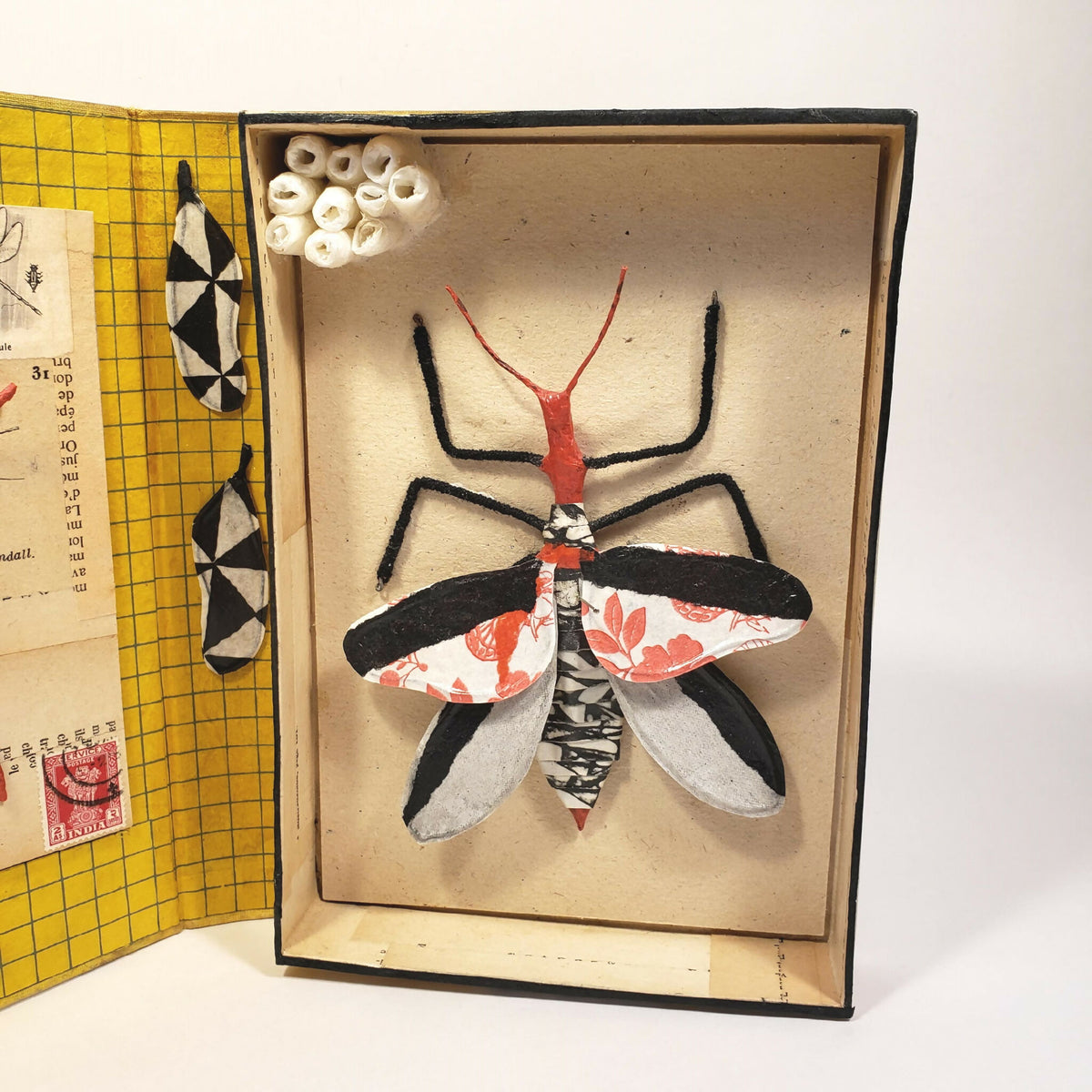 Livre jaune sculpté, insecte en relief sur la page intérieure droite, vue rapprochée.