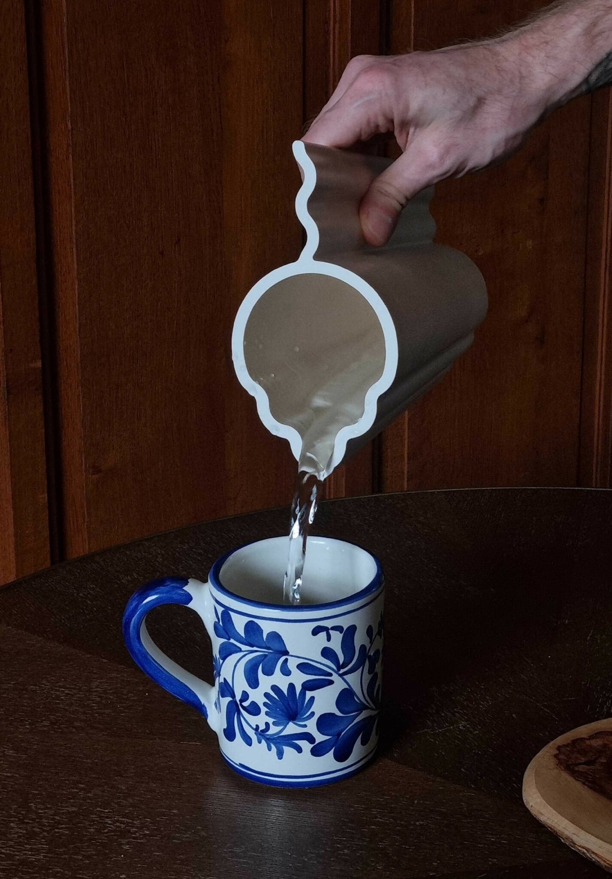 Vase blanc tenu à la main, versement d’un liquide dans une petite tasse bleue.