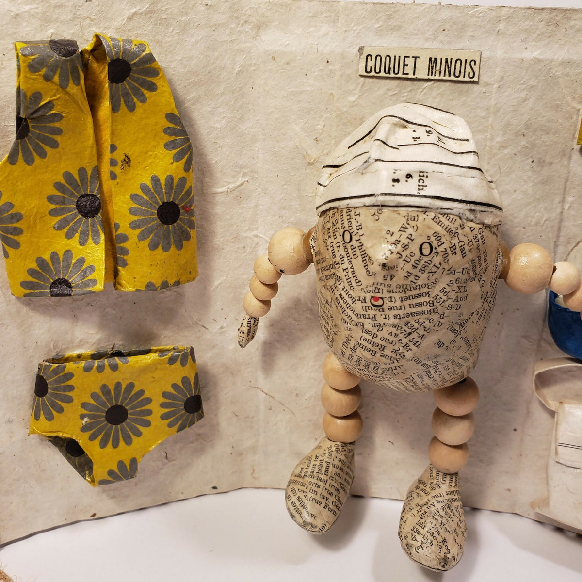 Sculpture Coquet minois : figurine sur panneau en carton, vêtements jaunes à motifs