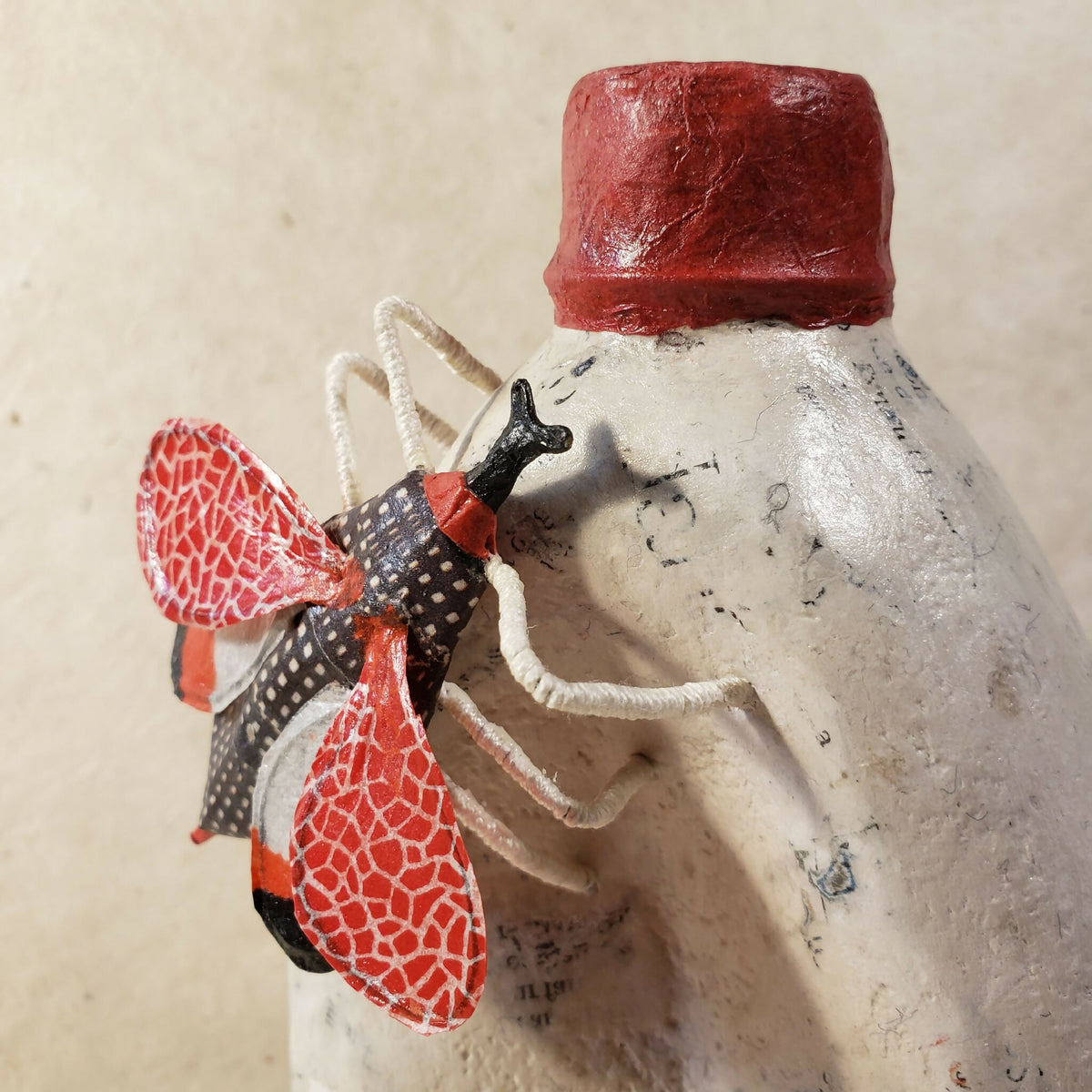 Sculpture de bouteille blanche, chapeau rouge et papillon rouge à pois noirs