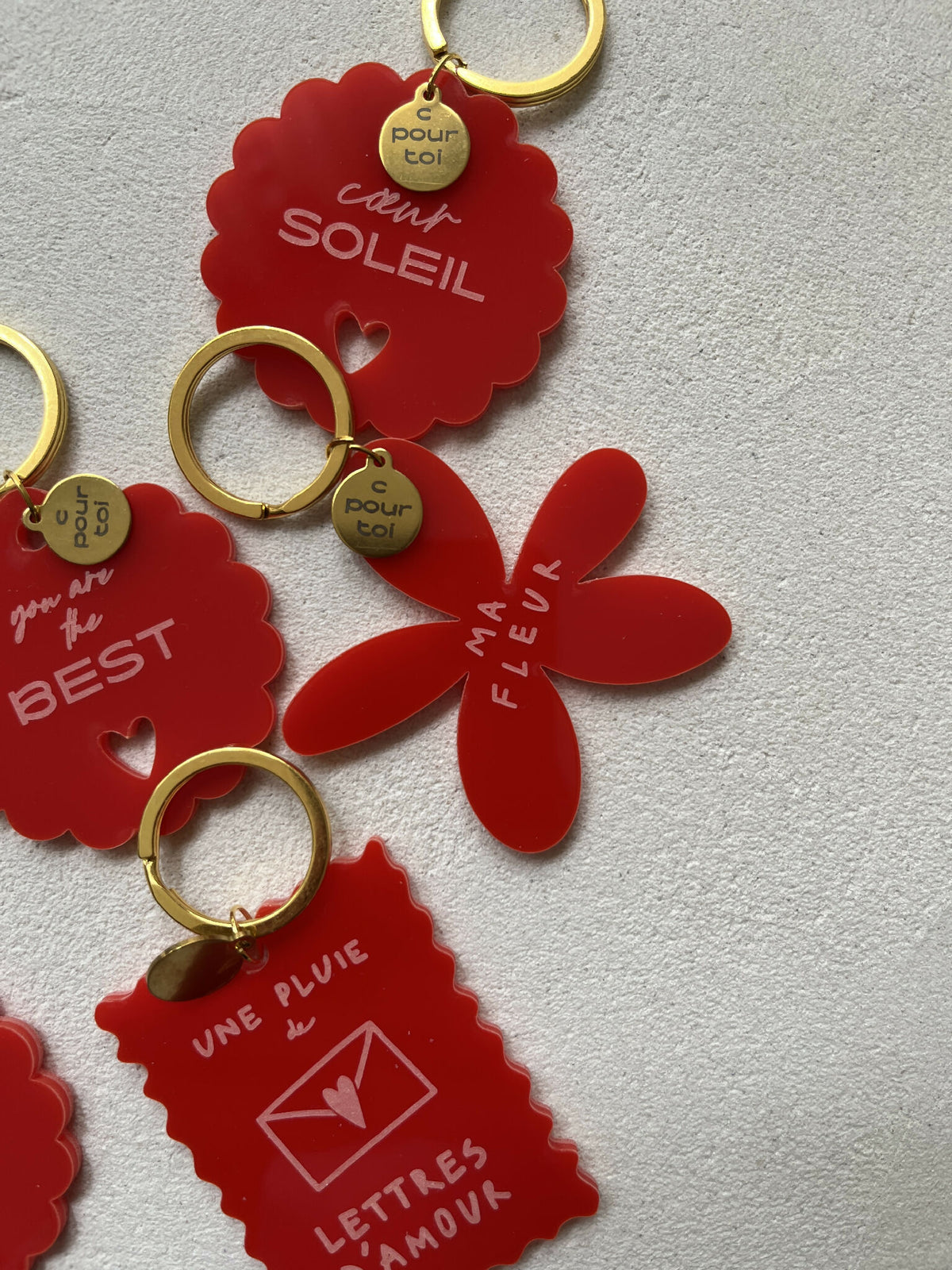 Porte-clés soleil rouges à anneaux dorés, textes gravés dont « BEST »