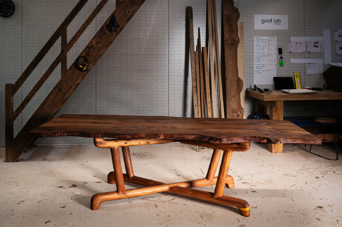 Table en bois massif avec plateau rustique et piètement en tréteaux arrondis.