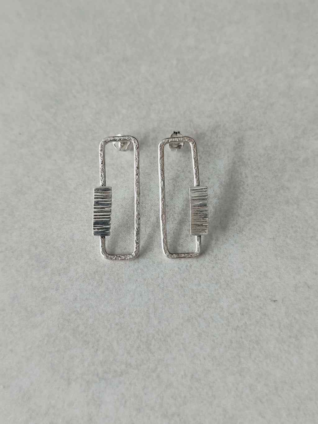 Boucles d’oreilles rectangulaires argentées, rayures verticales sur le centre.