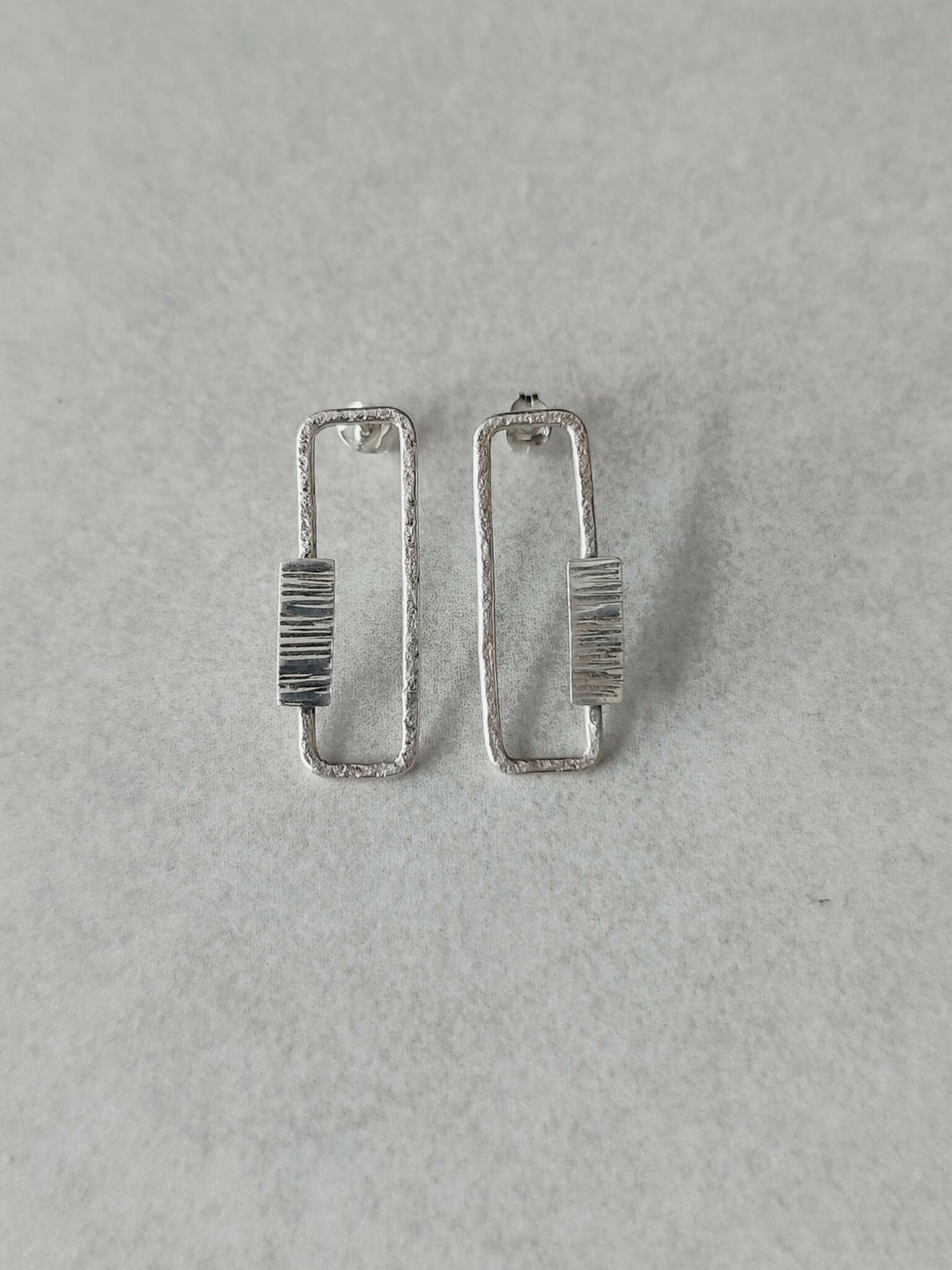 Boucles d’oreilles rectangulaires argentées, rayures verticales sur le centre.