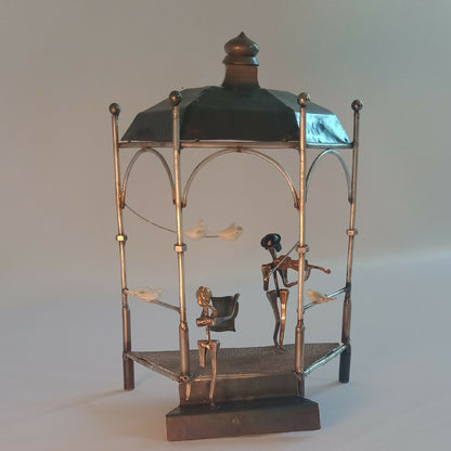 Cage de manège décorative en métal doré, toit noir et silhouettes peintes avec oiseaux.