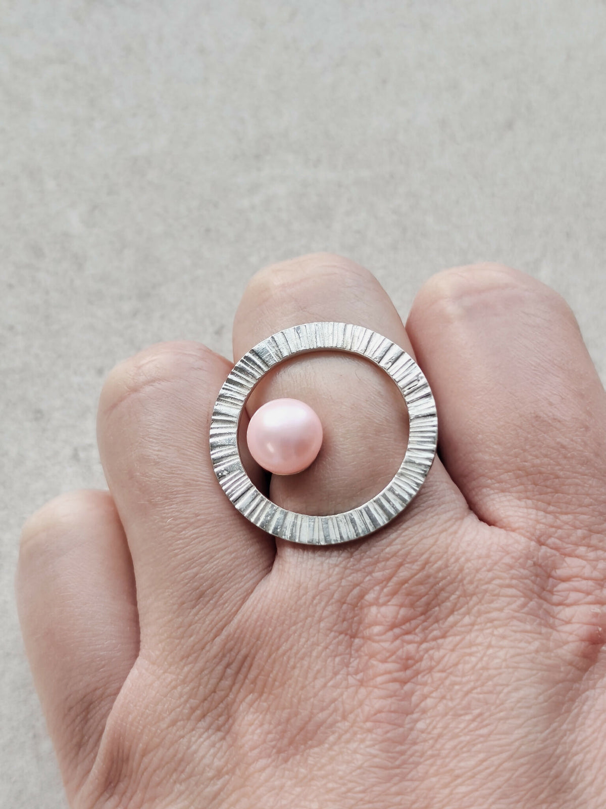 Bague Atoll cabochon perle rose sur anneau strié argenté, gros plan sur main