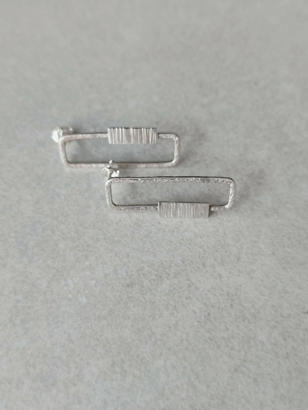 Boucles d’oreilles rectangulaires argentées, vue inclinée des rayures verticales.