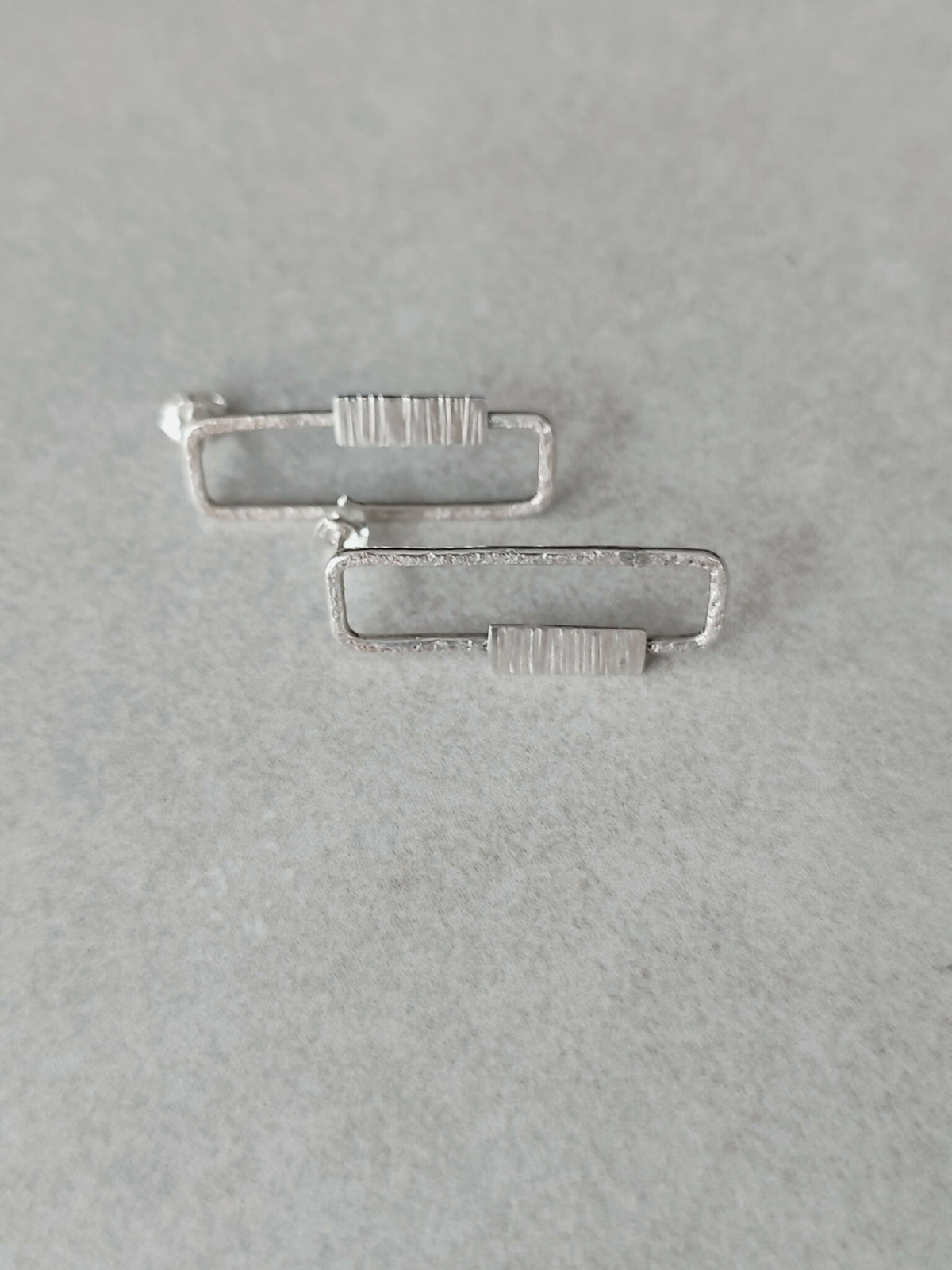 Boucles d’oreilles rectangulaires argentées, vue inclinée des rayures verticales.