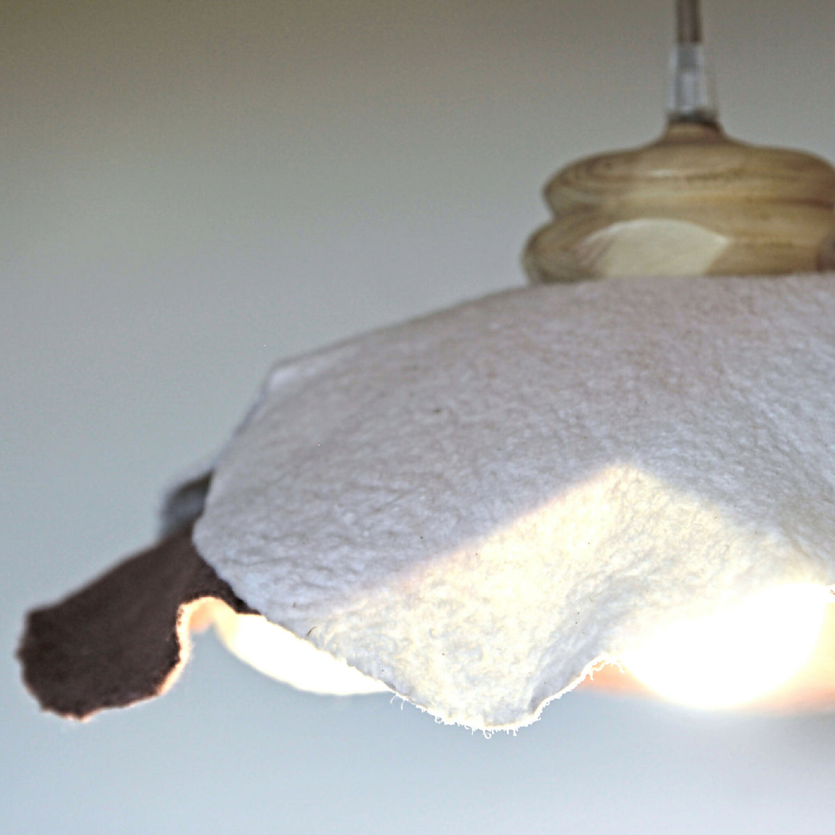 Abat-jour en laine feutrée blanche, bord marron découpé, lumière au centre