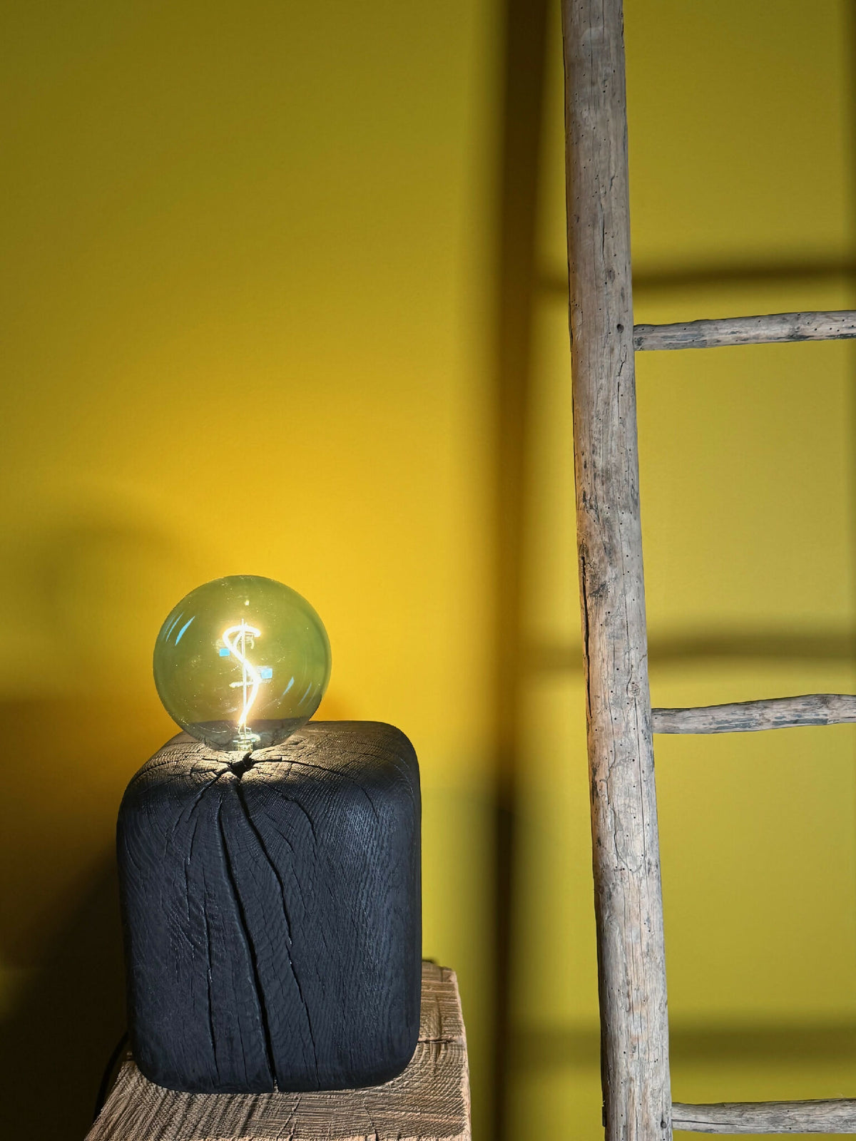 Sculpture lumineuse : ampoule sphérique vert émeraude sur base cubique bleu foncé.