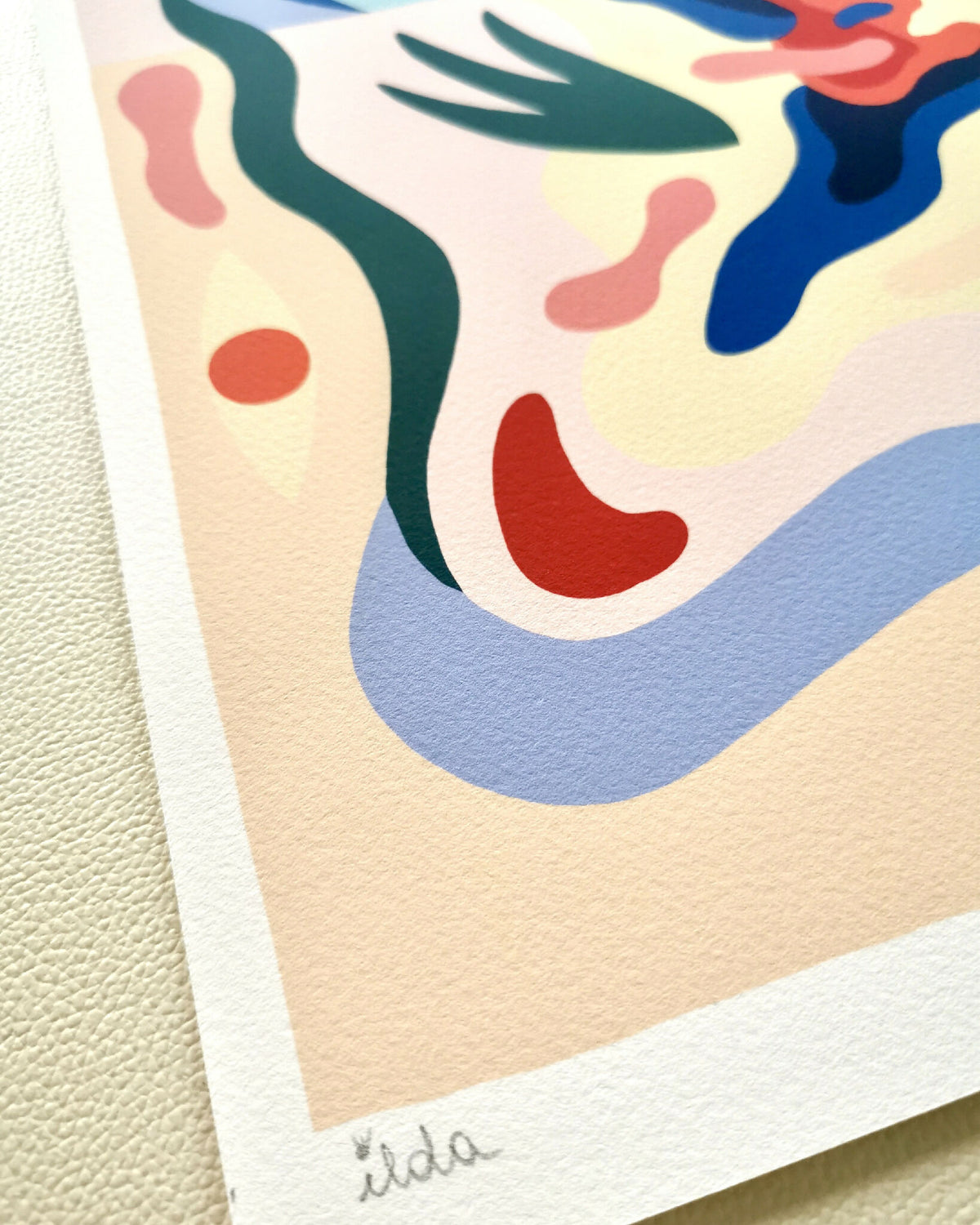 Détail d’affiche : papier texturé beige avec signature, motif abstrait bleu et vert.