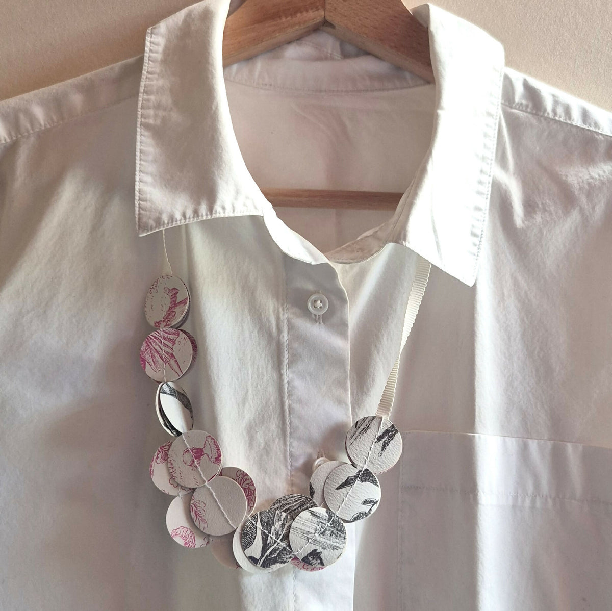 Collier en disques ronds noir, blanc et rose à motifs floraux, sur chemise blanche