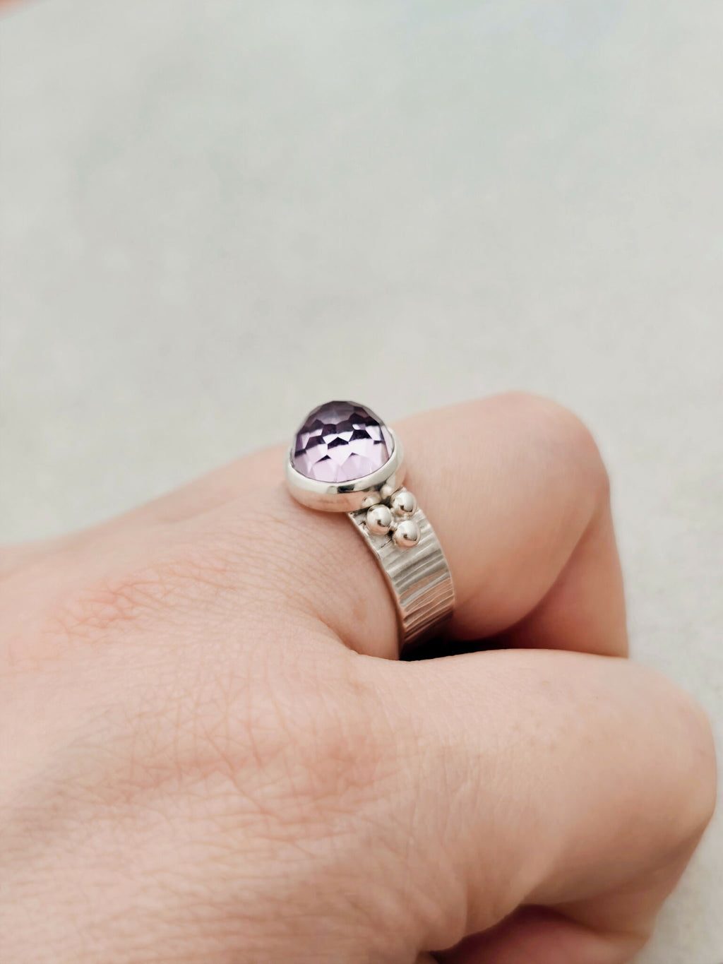 Bague argentée avec pierre améthyste violette facettée, détails décoratifs au côté.
