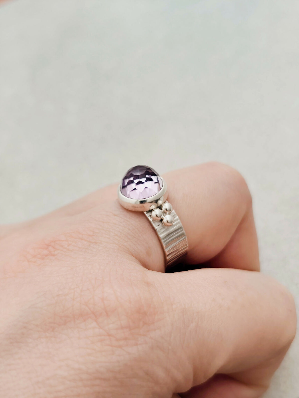 Bague argentée avec pierre améthyste violette facettée, détails décoratifs au côté.