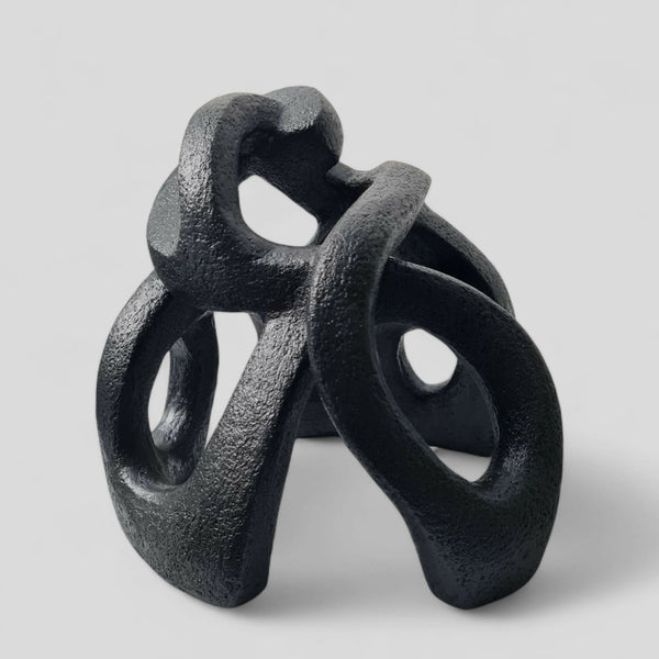 Sculpture abstraite contemporaine en matériau sombre, formes entrelacées avec ouvertures