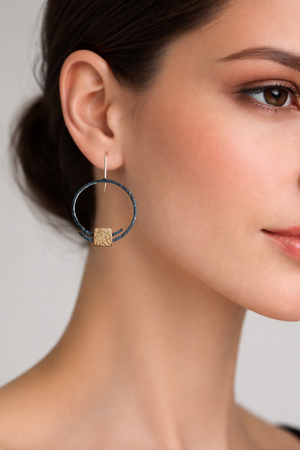Boucles d’oreilles pendantes sur l’oreille : anneau noir et carré doré texturé.