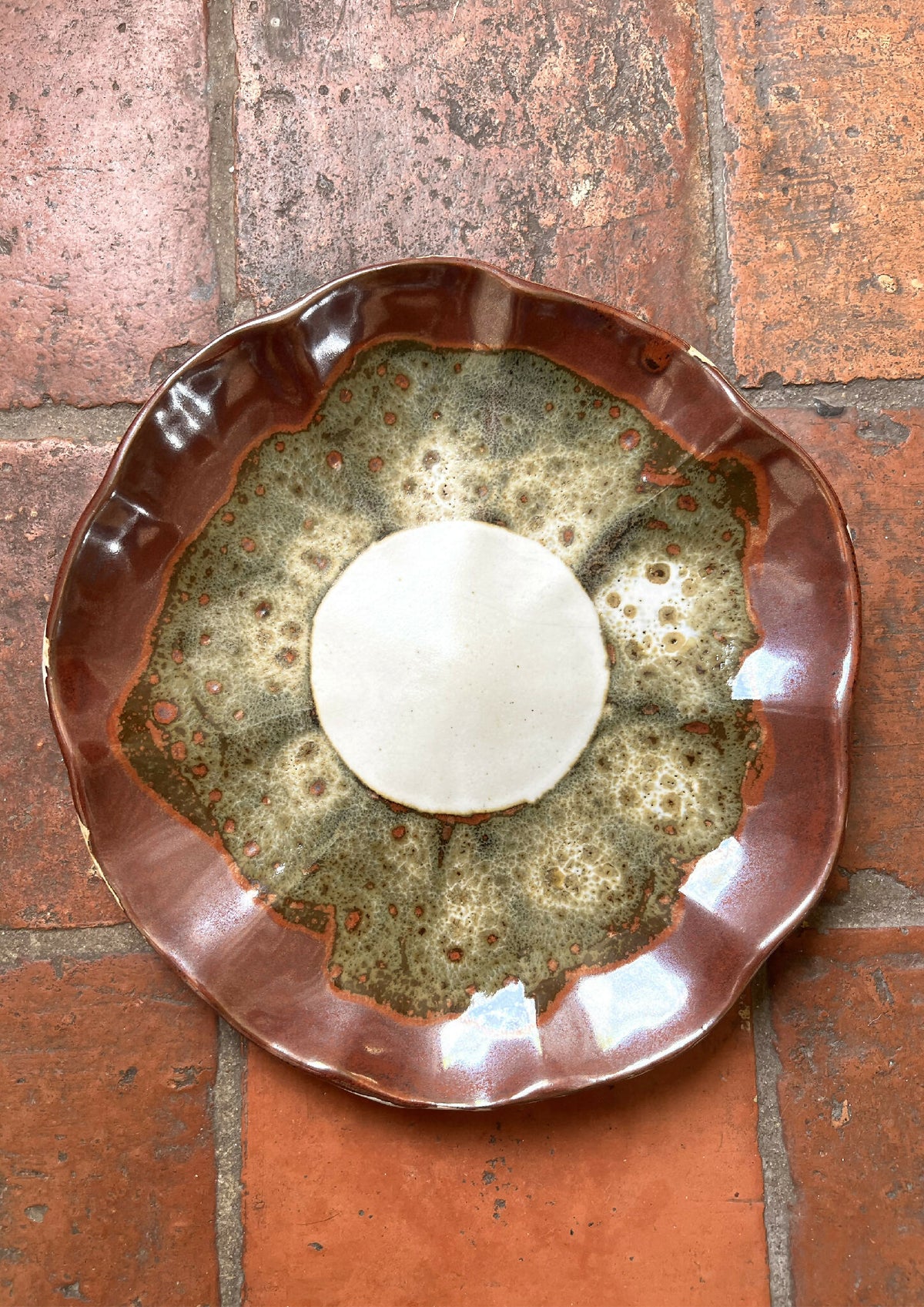 Assiette Prunelle à bord brun, centre vert moucheté et éclats rouges, motif évasé.