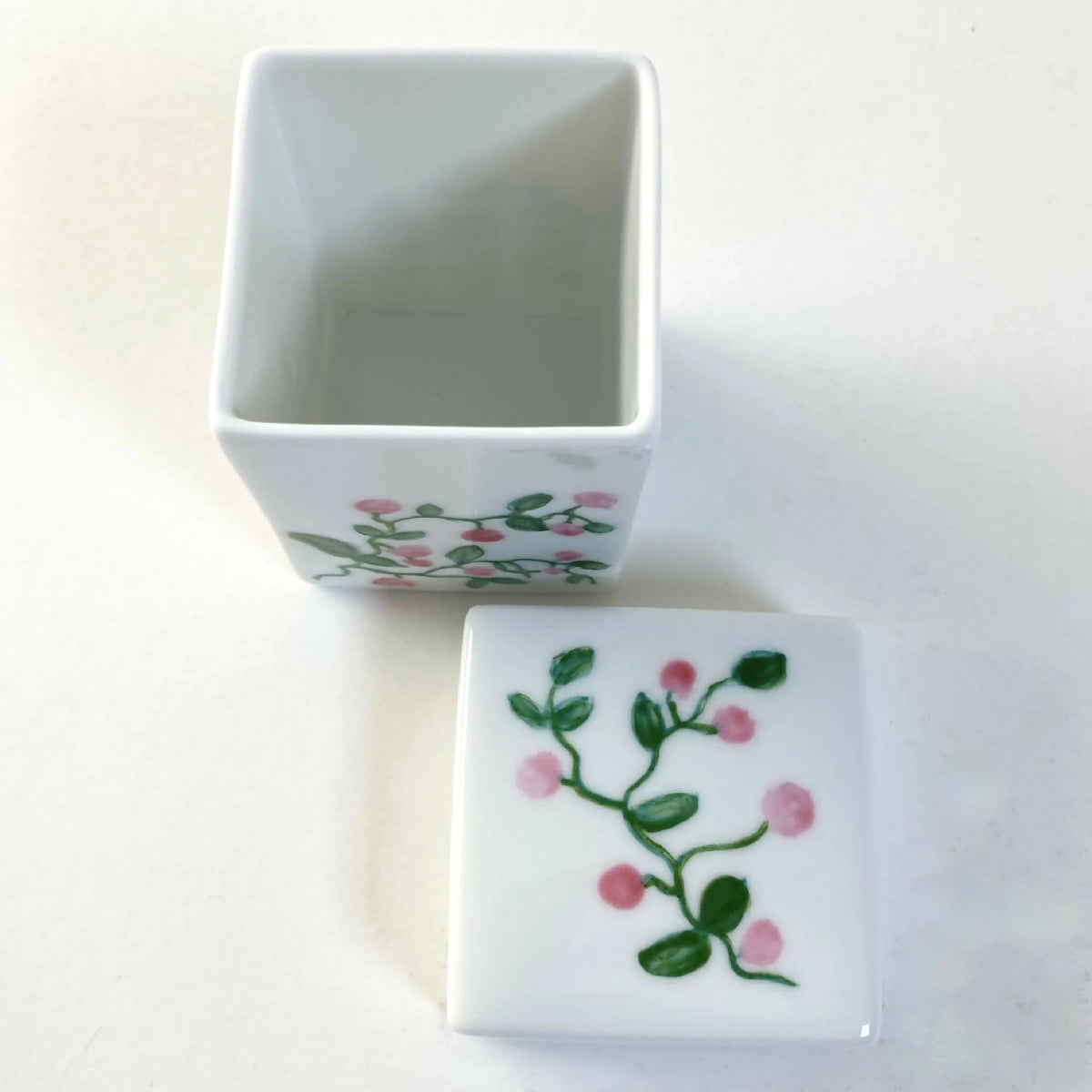 Boîte à bijoux en porcelaine blanche, couvercle ouvert, motif floral rose.