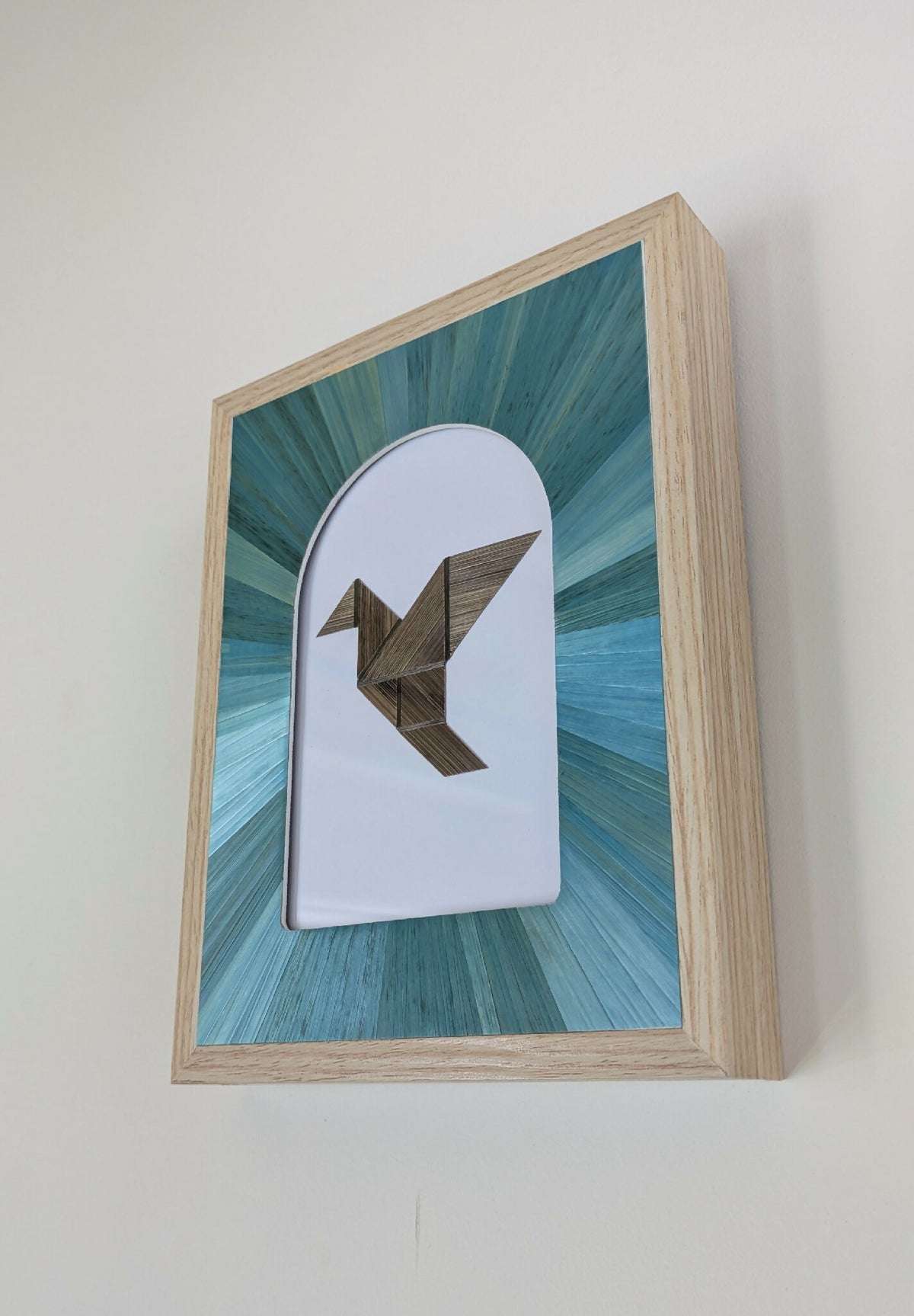 Tableau marqueterie en paille : oiseau géométrique brun sur fond turquoise, cadre beige.