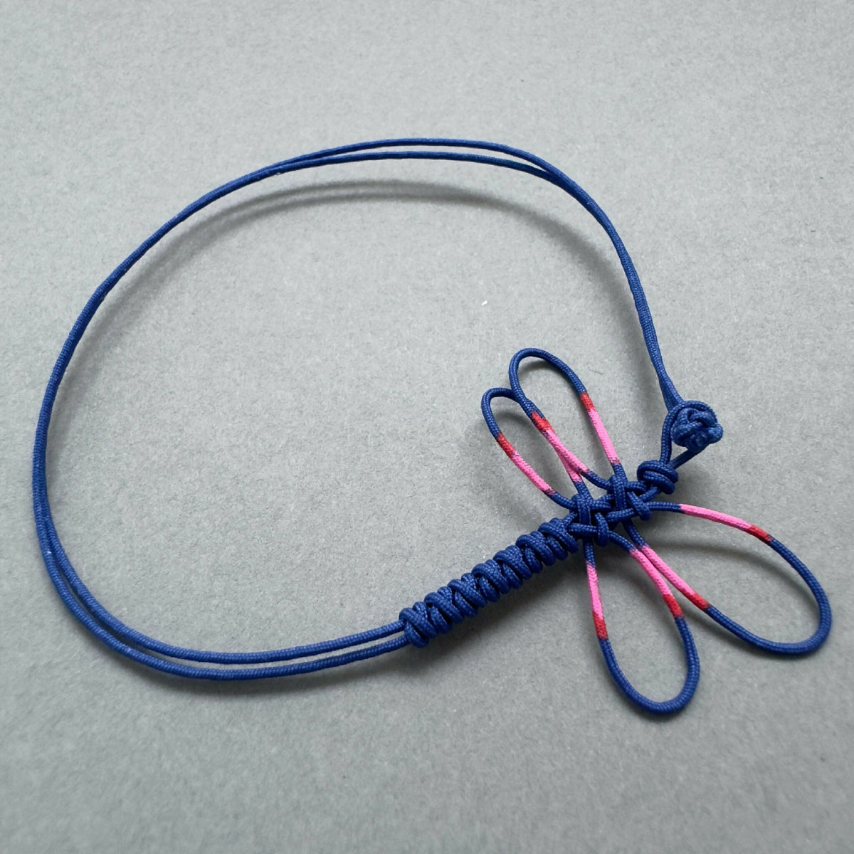 Bracelet bleu circulaire avec motif de libellule rose en relief, cordons noués.