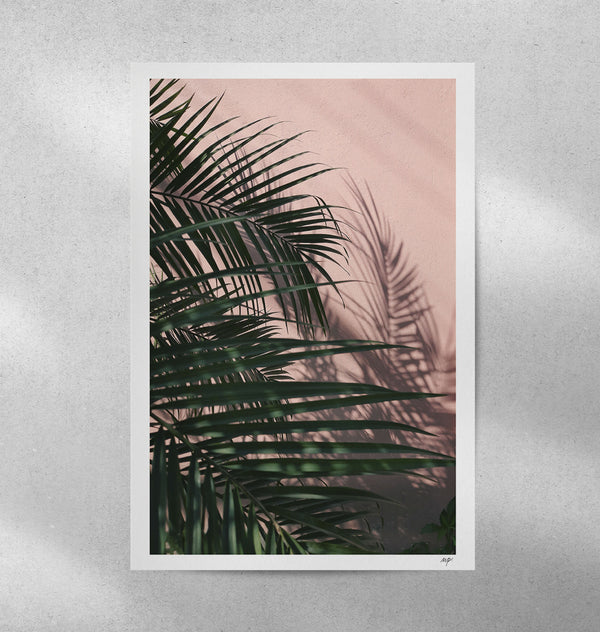 Tirage d’art avec feuillage de palmier vert foncé sur fond rose clair, bord blanc