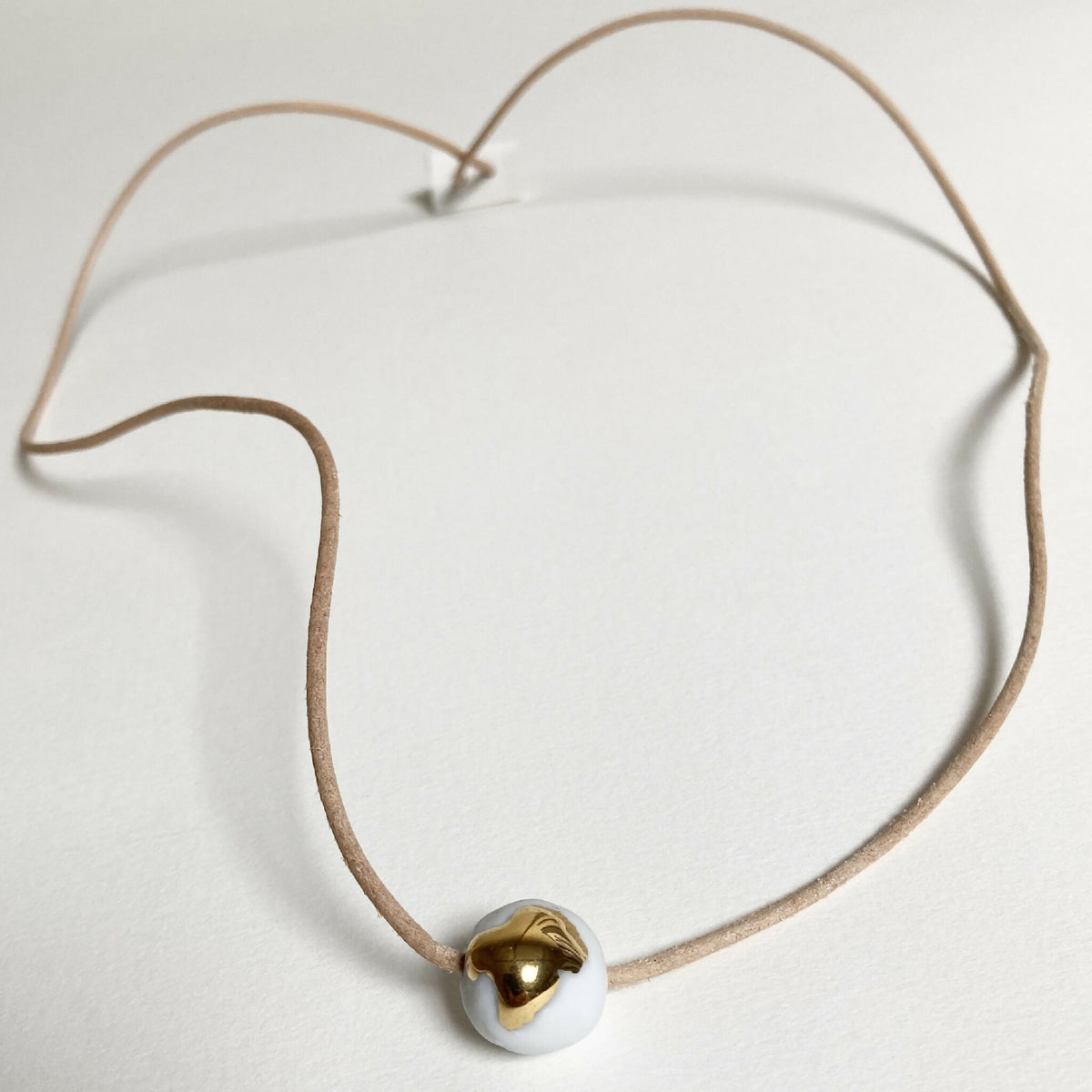 Collier en porcelaine à pendentif rond doré, cordon marron et base claire.
