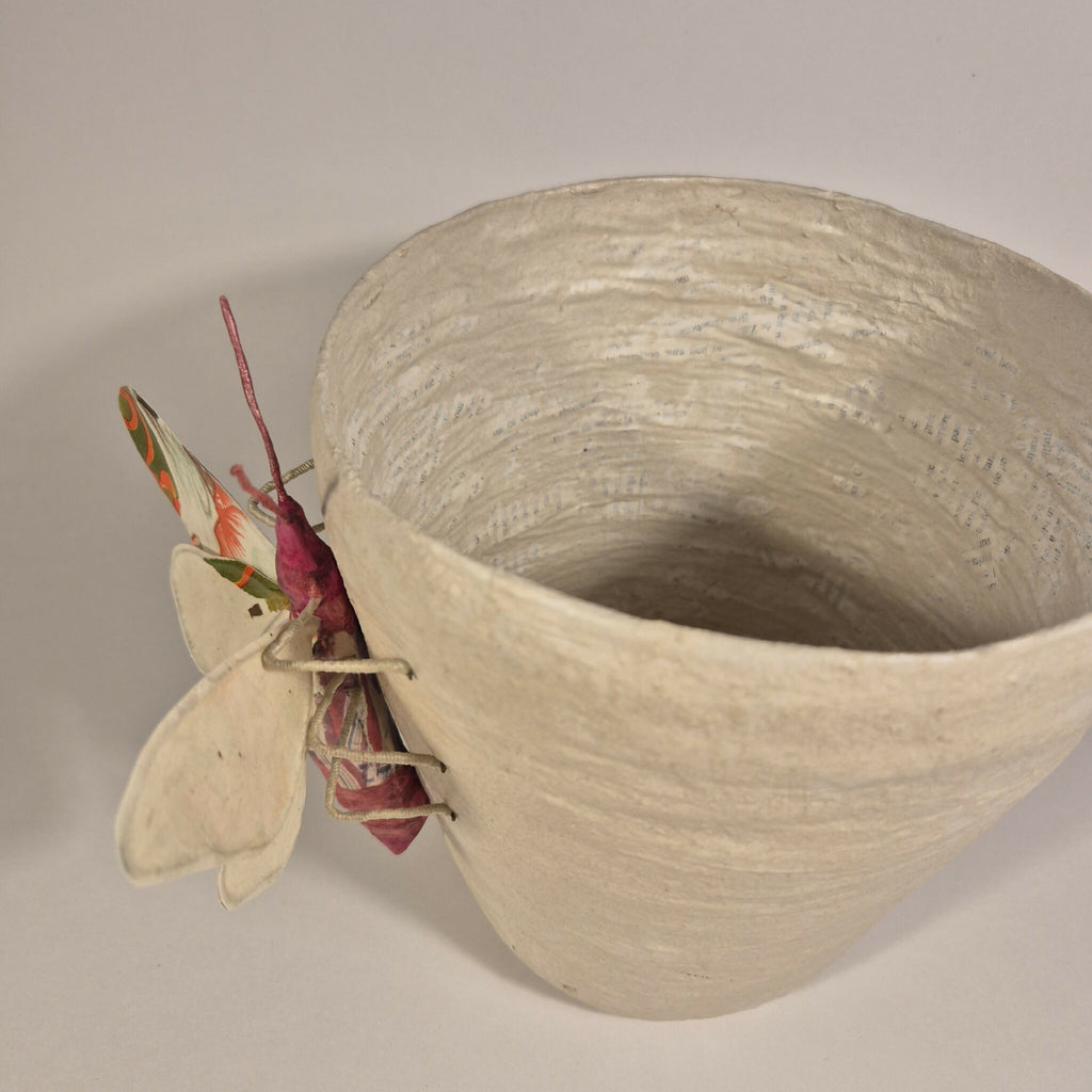 Sculpture de papillon multicolore sur pot en béton clair, profil près de l’ouverture
