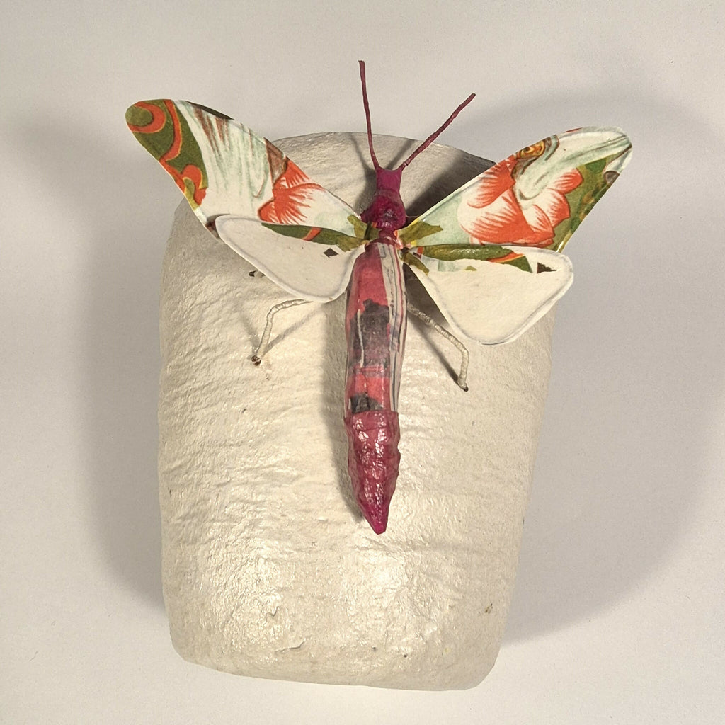 Sculpture de papillon multicolore sur pot en béton clair, vue avant avec ailes ouvertes