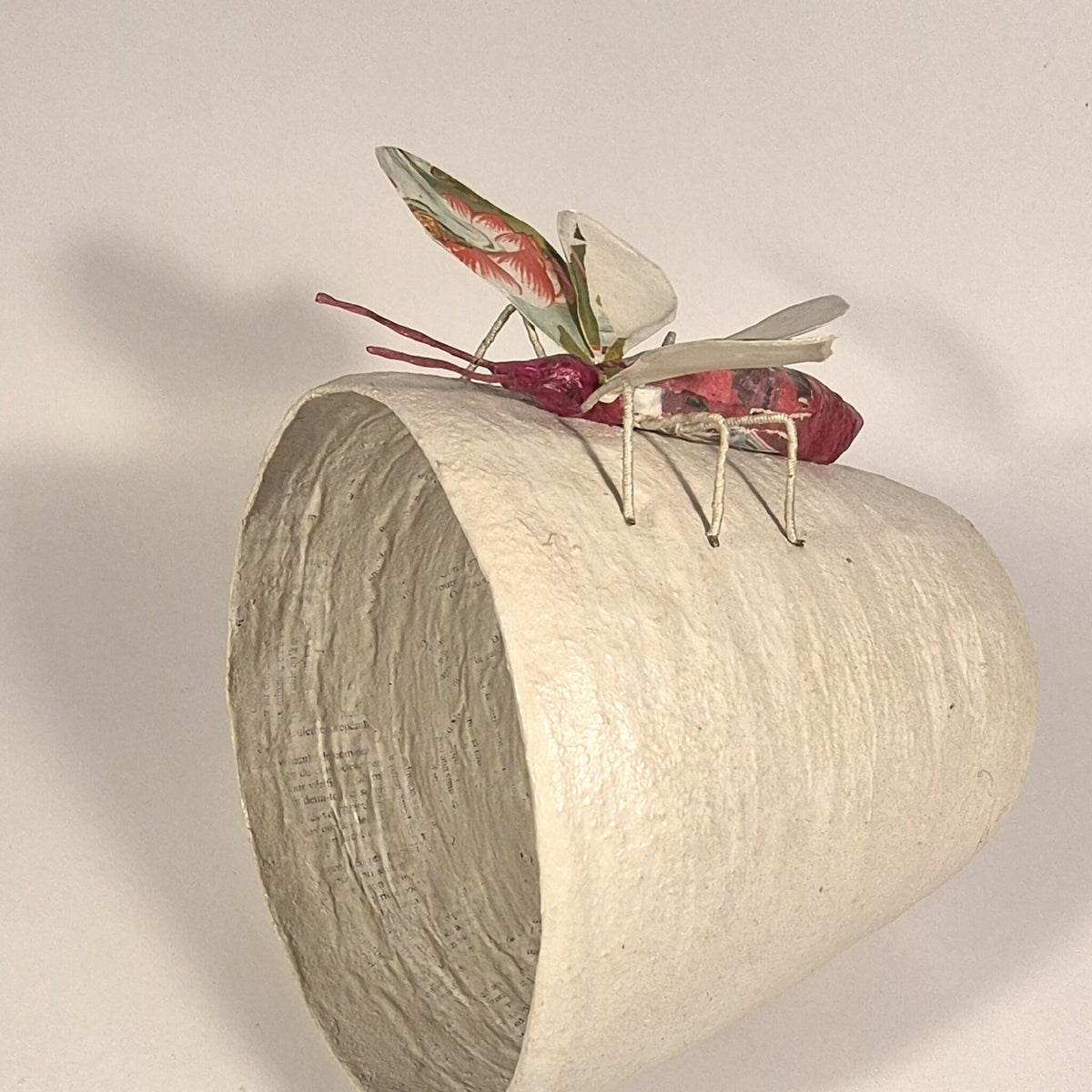 Sculpture de papillon multicolore sur pot en béton clair, vue de côté avec antennes
