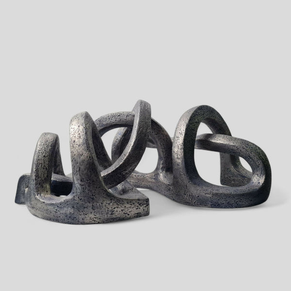 Sculpture abstraite sur base, courbes enchevêtrées gris bleuté au fini granuleux.