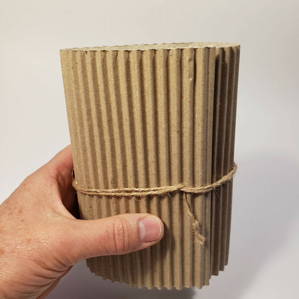 Tube en carton ondulé beige tenu par la main, ficelle autour