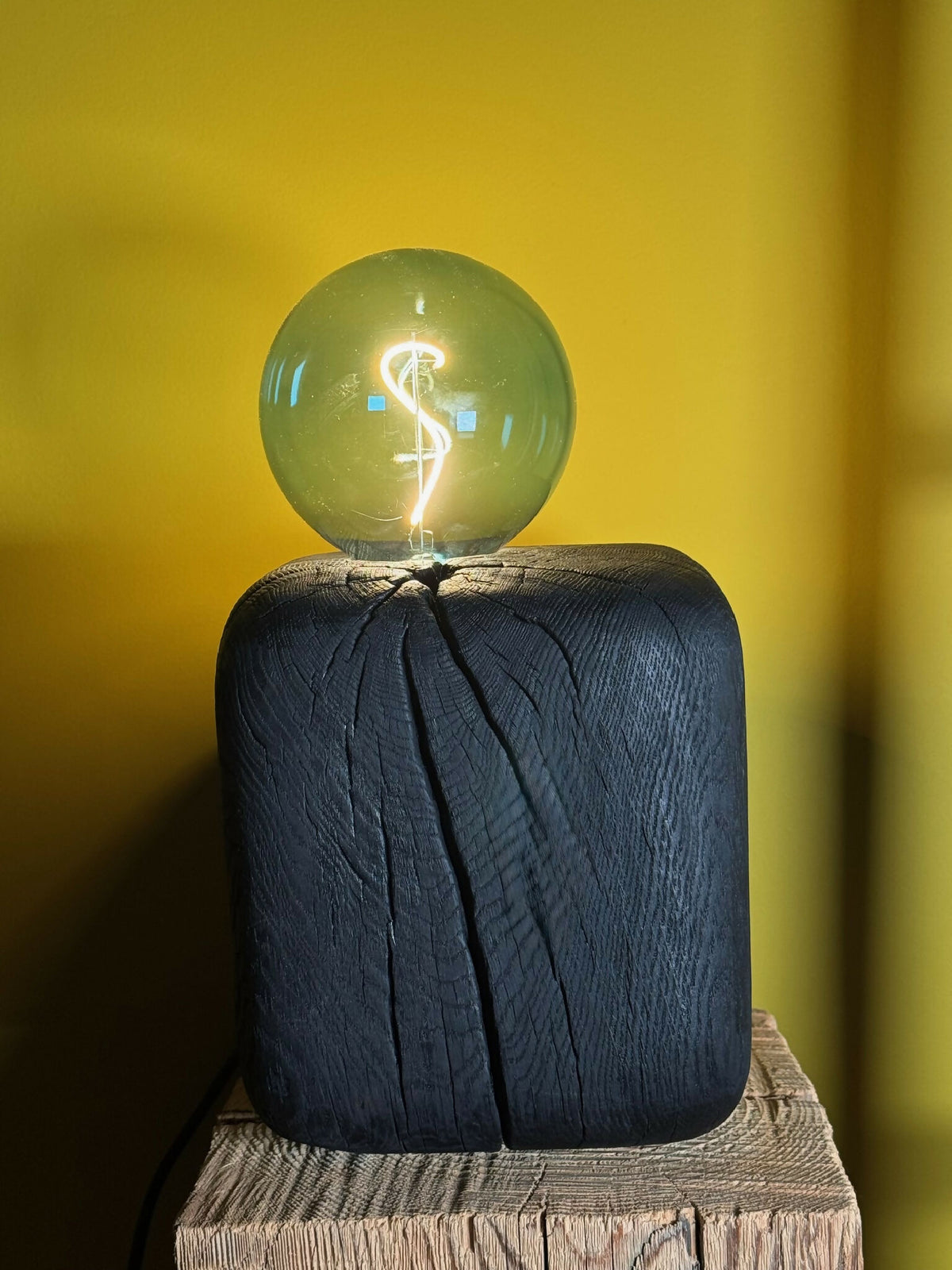Sculpture lumineuse : ampoule sphérique vert émeraude sur base cubique bleu foncé texturée.