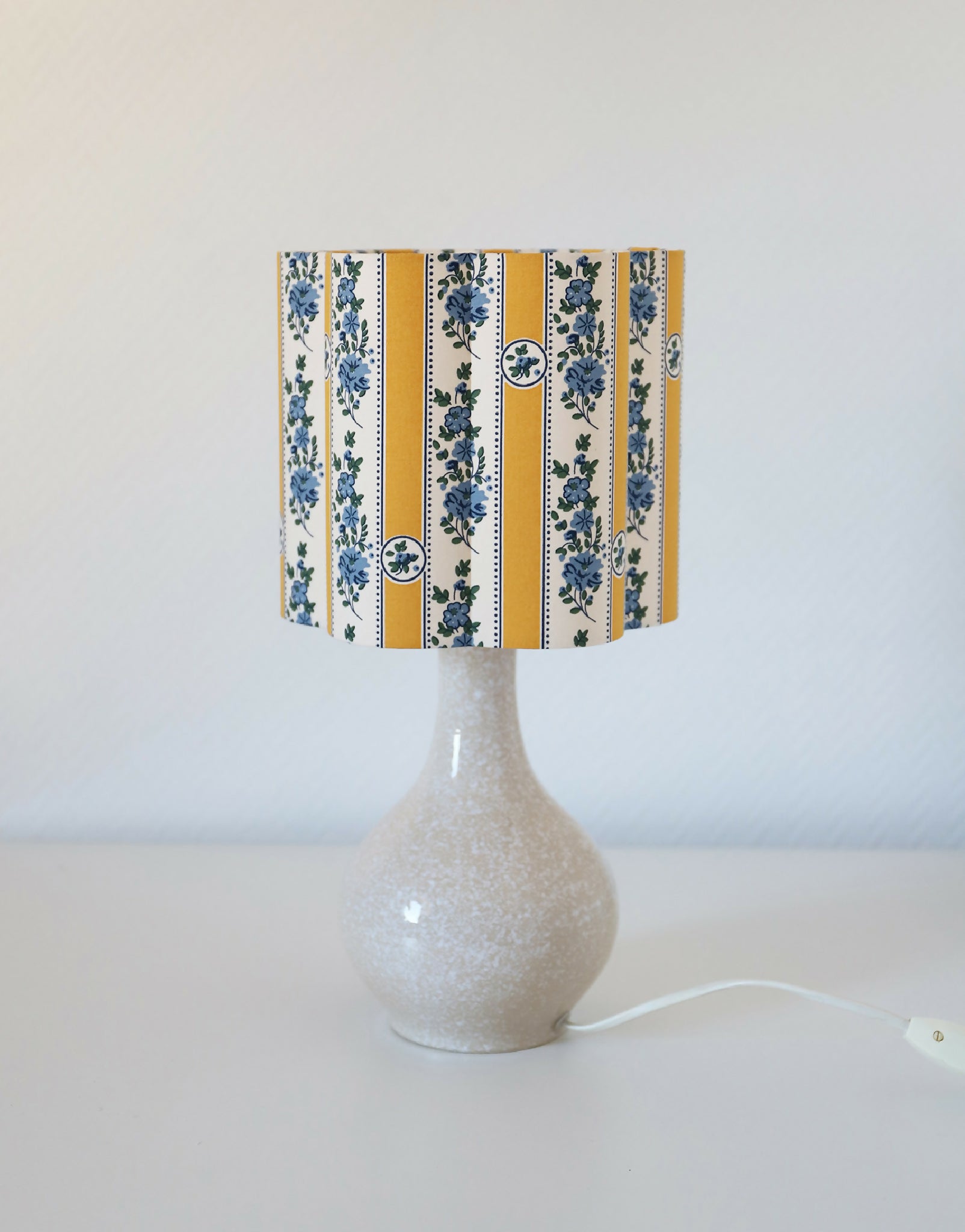 Abat-jour forme fleur rayé jaune et bleu posé sur pied de lampe.