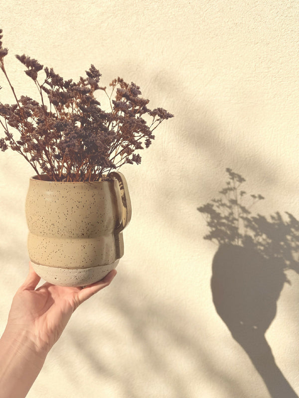 Vase en céramique beige moucheté avec anses, tenu à la main