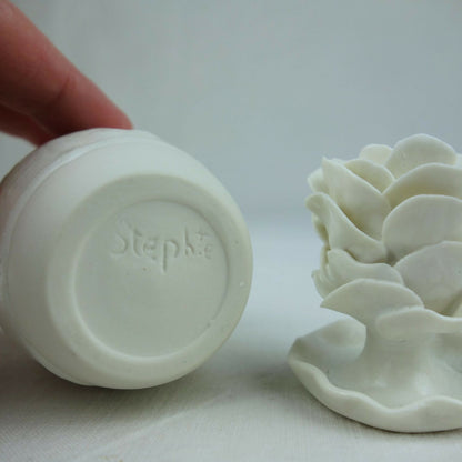 Base en céramique blanc avec marquage au fond et petite fleur en relief à côté.