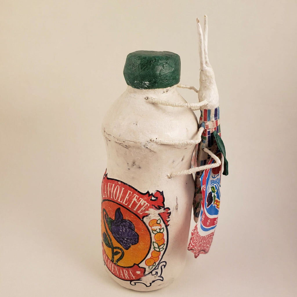 Sculpture posée sur une bouteille, profil, capuchon vert, motifs colorés et sangles autour du cou